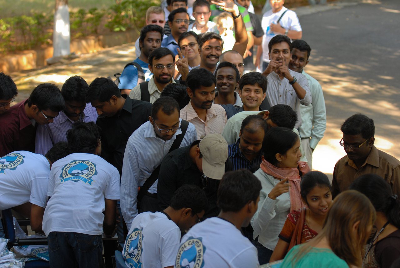 A large group of people waits in line at the Drupalcamp Deccan registration table, assisted by event volunteers.