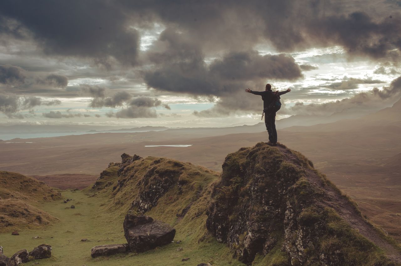 A person standing on a rock, arms wide open, overlooking a vast landscape.