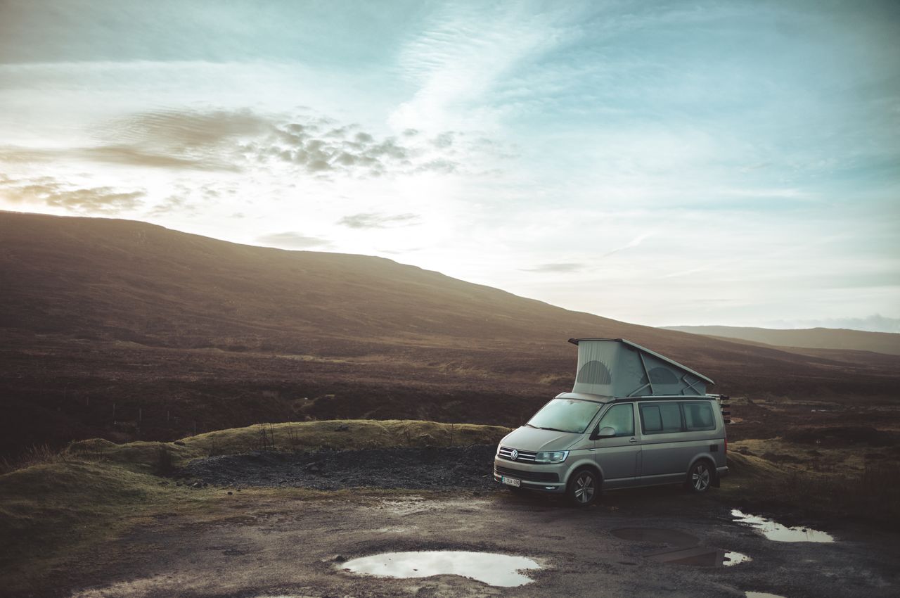 A parked camper van with a raised roof sitting in an open landscape.