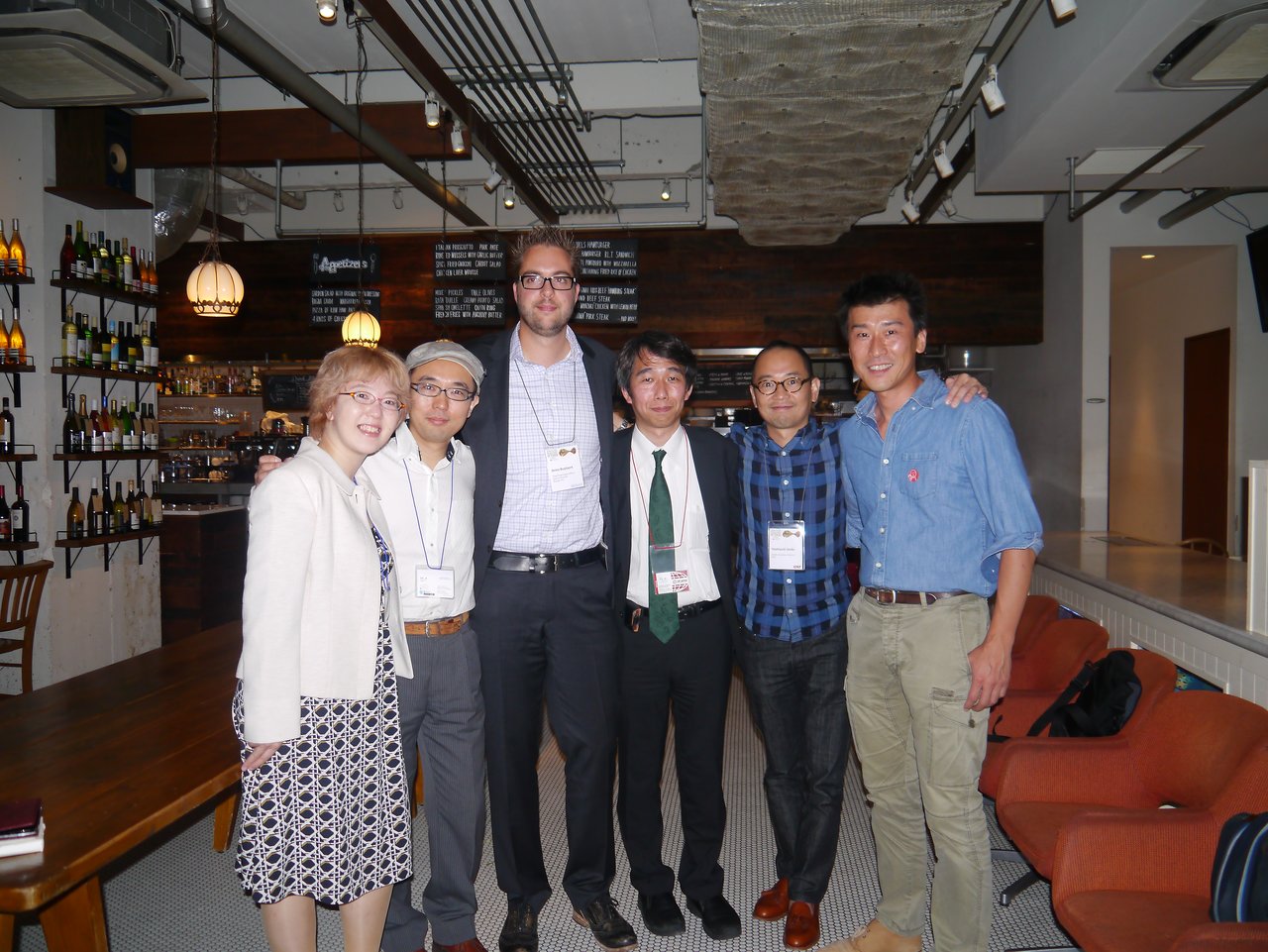 A group of six people posing together in a restaurant, dressed in business and casual attire, wearing name tags.