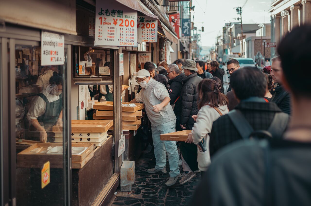 A crowd gathers outside a busy mochi shop in Nara, Japan, where workers in aprons hand out fresh rice cakes to waiting customers.
