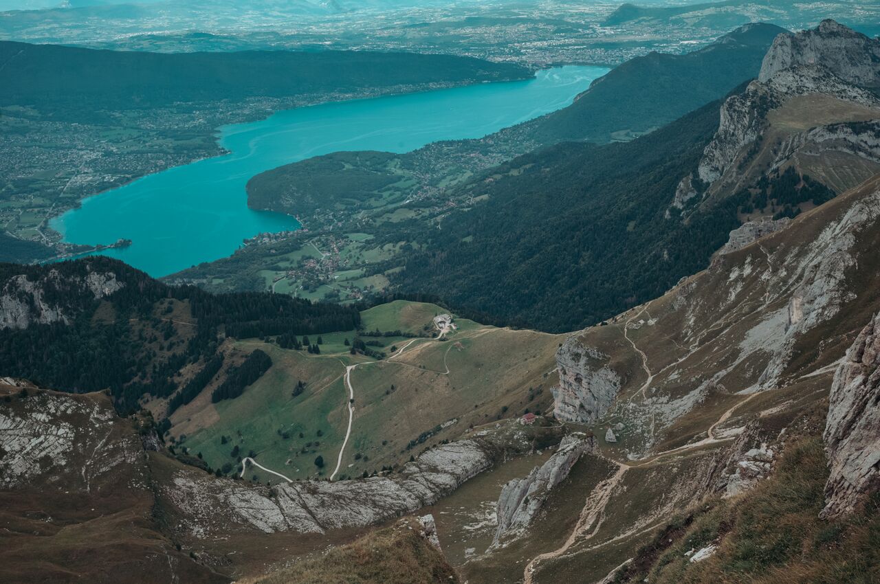 View over Lake Annecy from La Tournette trail, with switchback paths, cliffs, forest near Col de la Forclaz, Chalet de l'Aulp, and old Refuge de la Tournette.