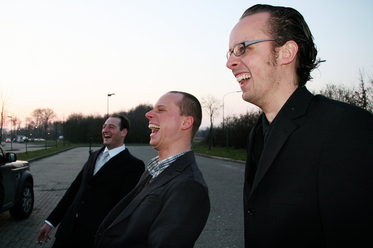 Three men in suits stand outside, laughing together during a bachelor party.