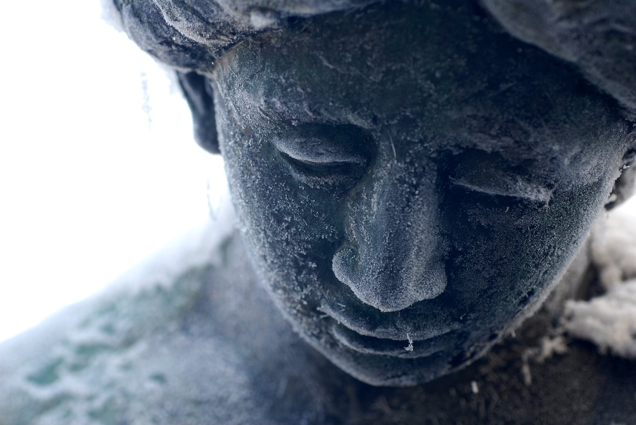 Close-up of a statue's face covered in frost, with ice crystals forming on the surface.