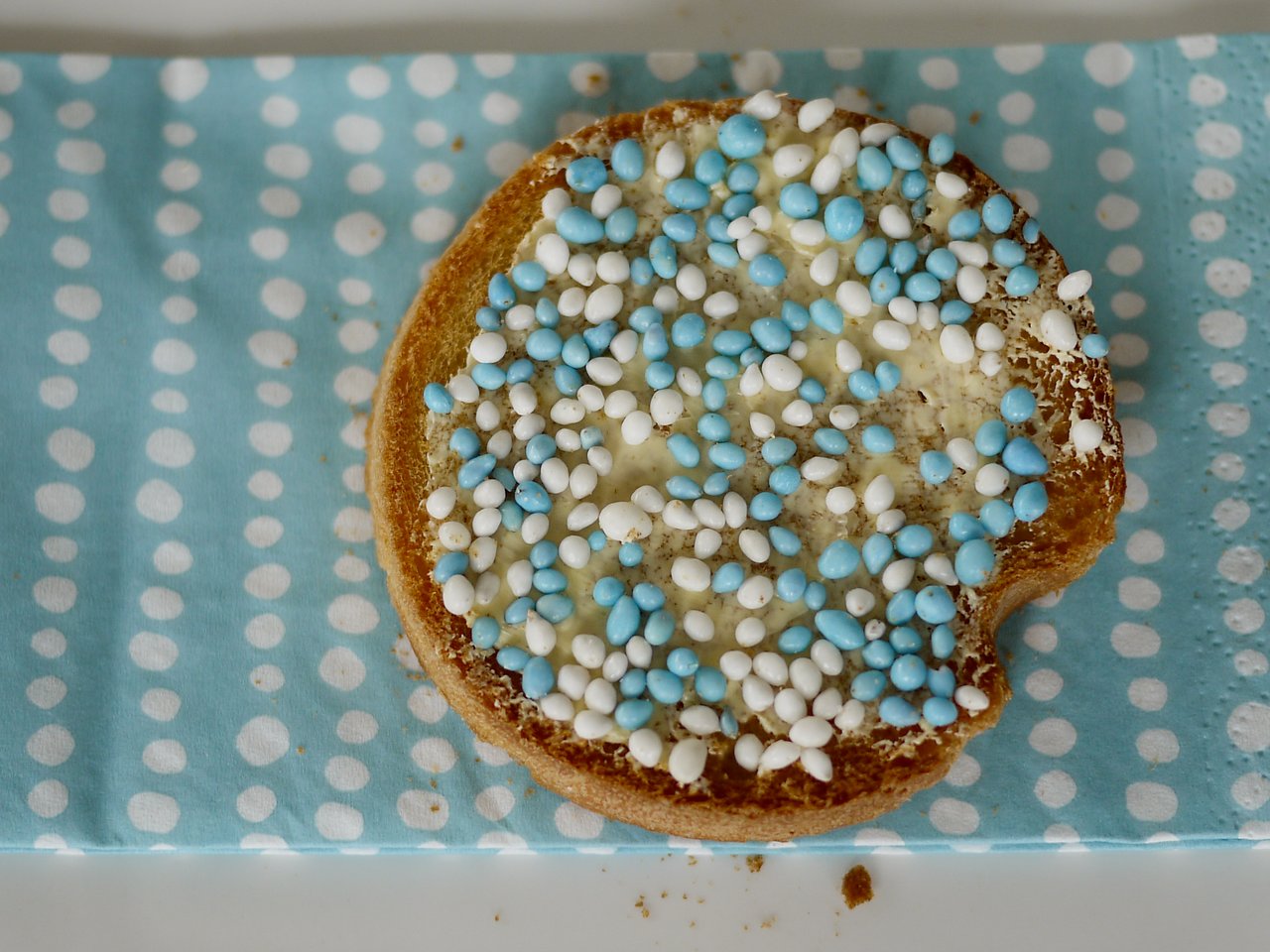 A piece of Dutch rusk with butter and blue-and-white sugar sprinkles on a polka-dotted napkin.