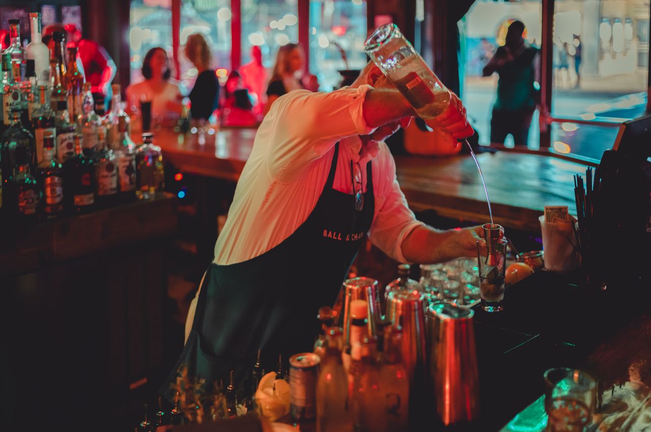 A bartender making a Mojito, pouring it from high above the glass.