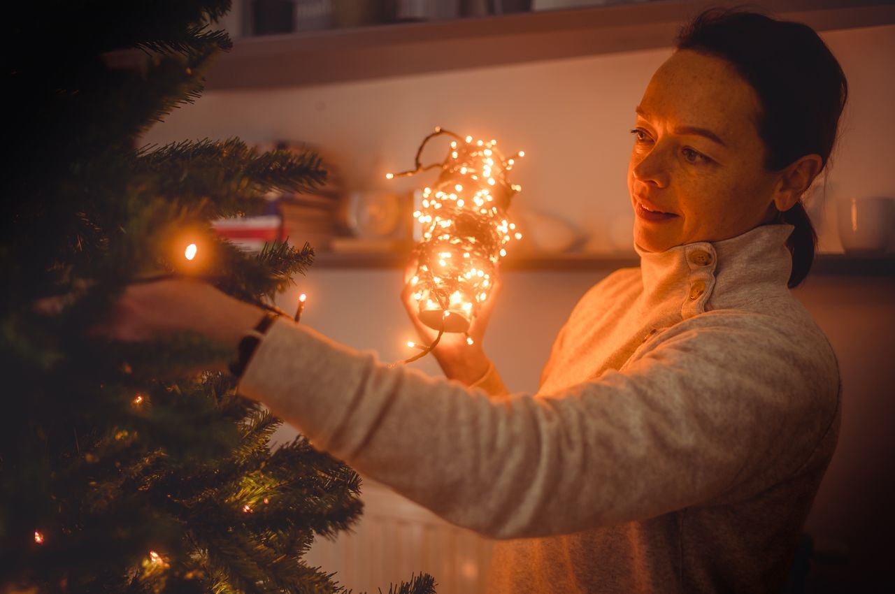 Vanessa carefully hangs lights on the branches of a Christmas tree, bringing a warm glow to the room.