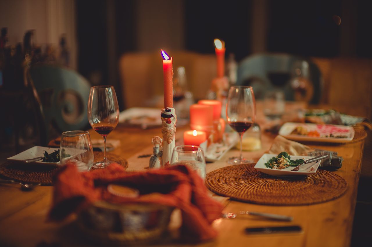 A table with the remnants of a meal, dirty plates, half-empty wine glasses, and candles that have half-way burned down, a testament to a lively and enjoyable gathering.