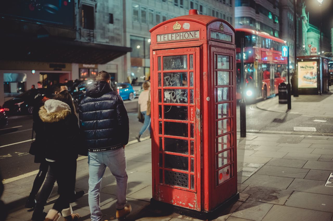 A group of young people stroll past a phone booth in London.