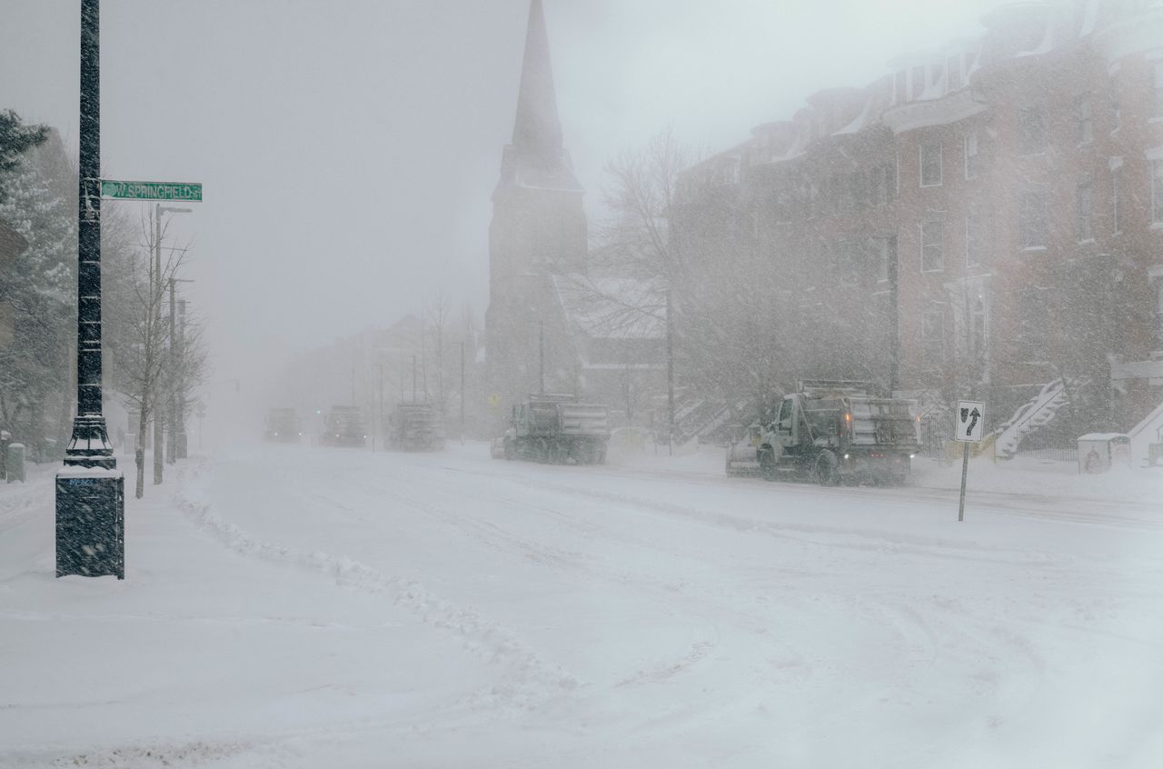 Five snow plows driving behind each other during a Boston snowstorm.