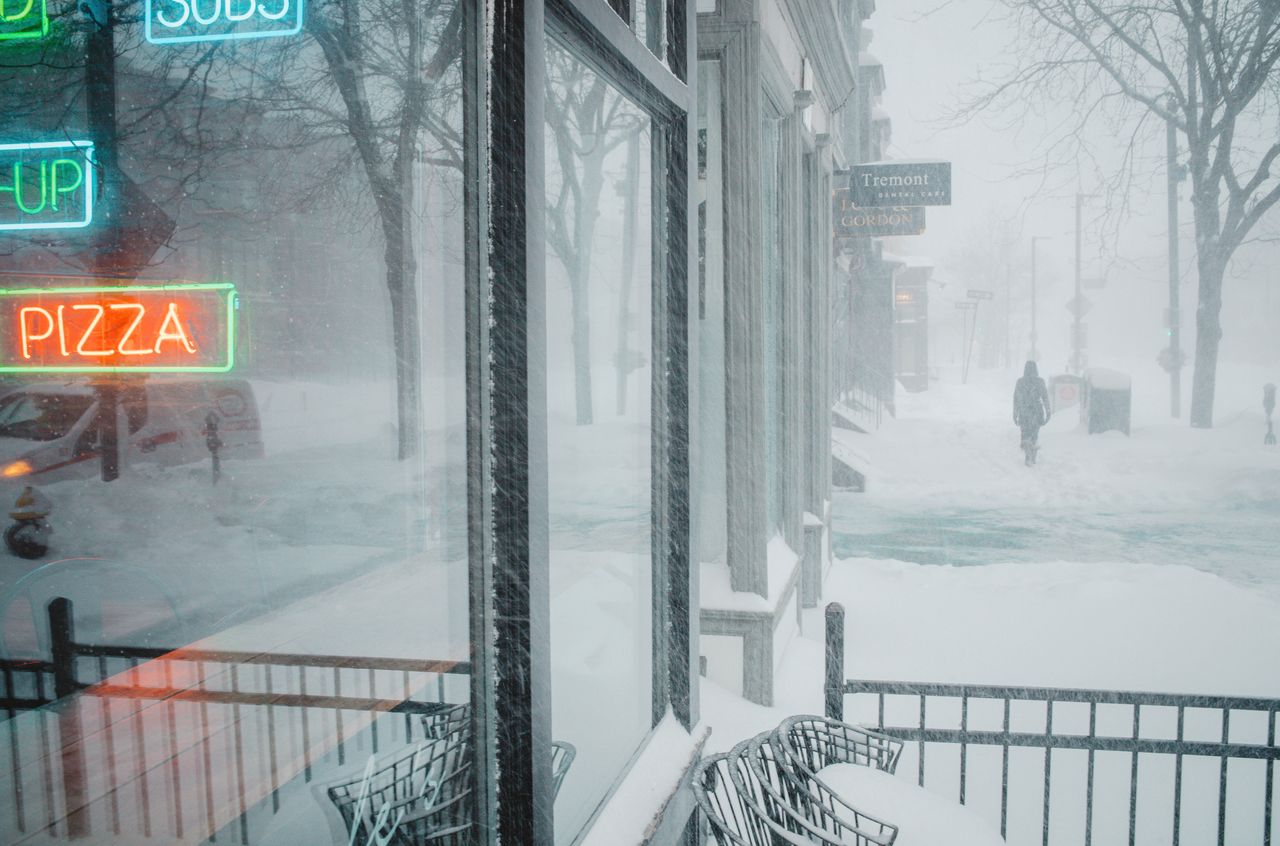 A snowy street with a pizza sign on the side of it.