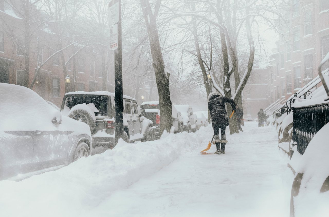 A woman shoveling snow on a sidewalk.