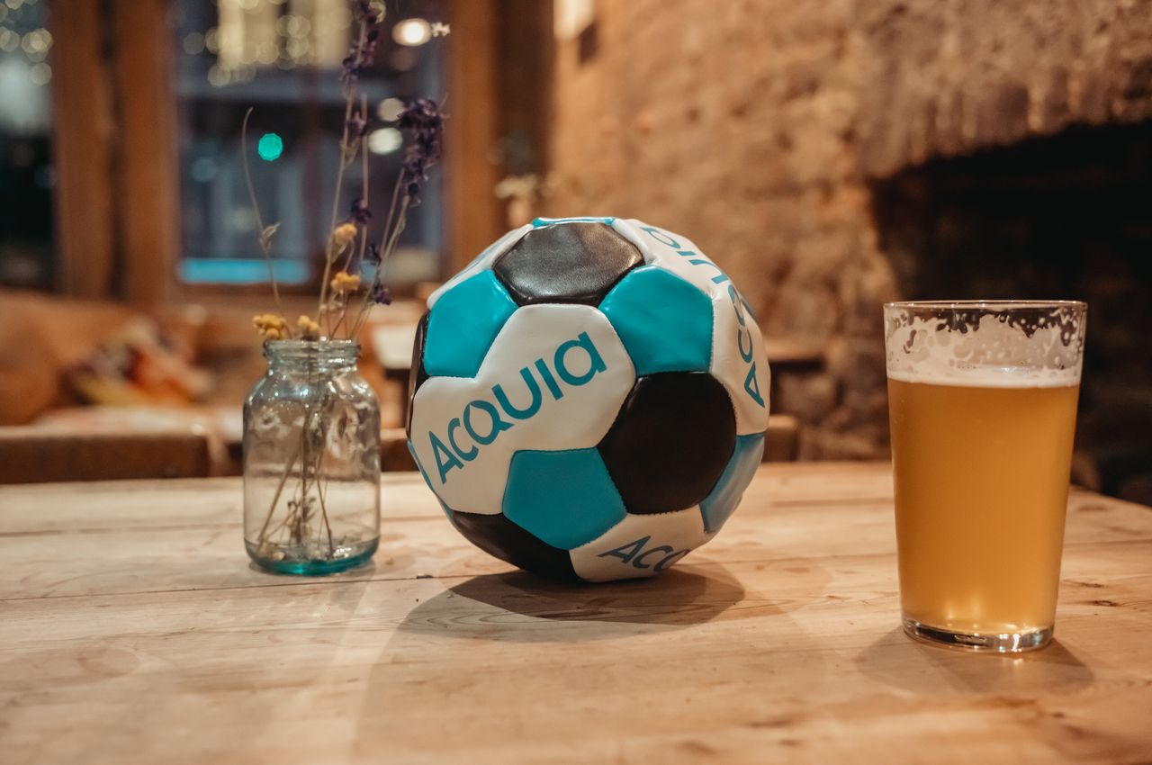 An Acquia-branded soccer ball and beer on a table in a pub.