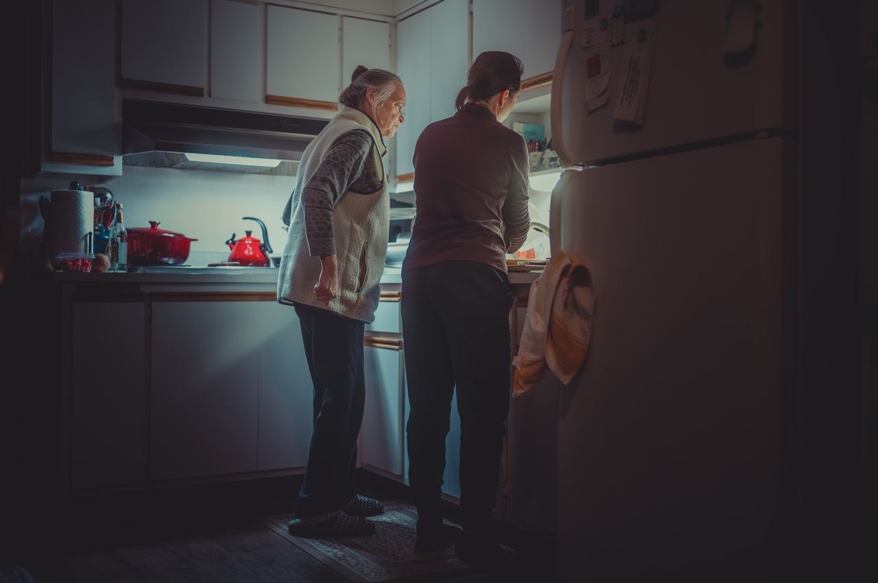A mother and daughter working together in a dimly lit kitchen.
