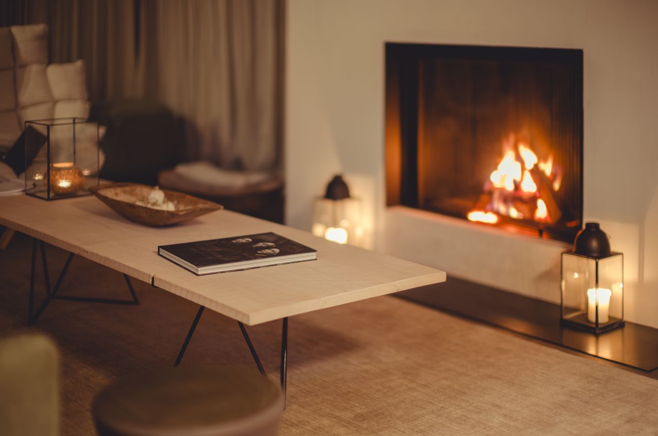 Cozy living room with a lit fireplace, candles, and a coffee table displaying a book.
