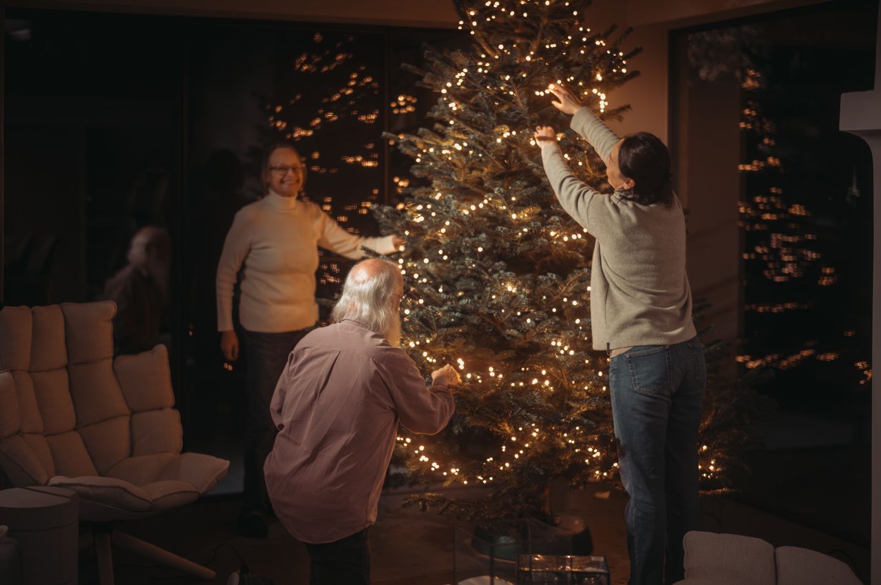 A family hanging the lights on a Christmas tree.