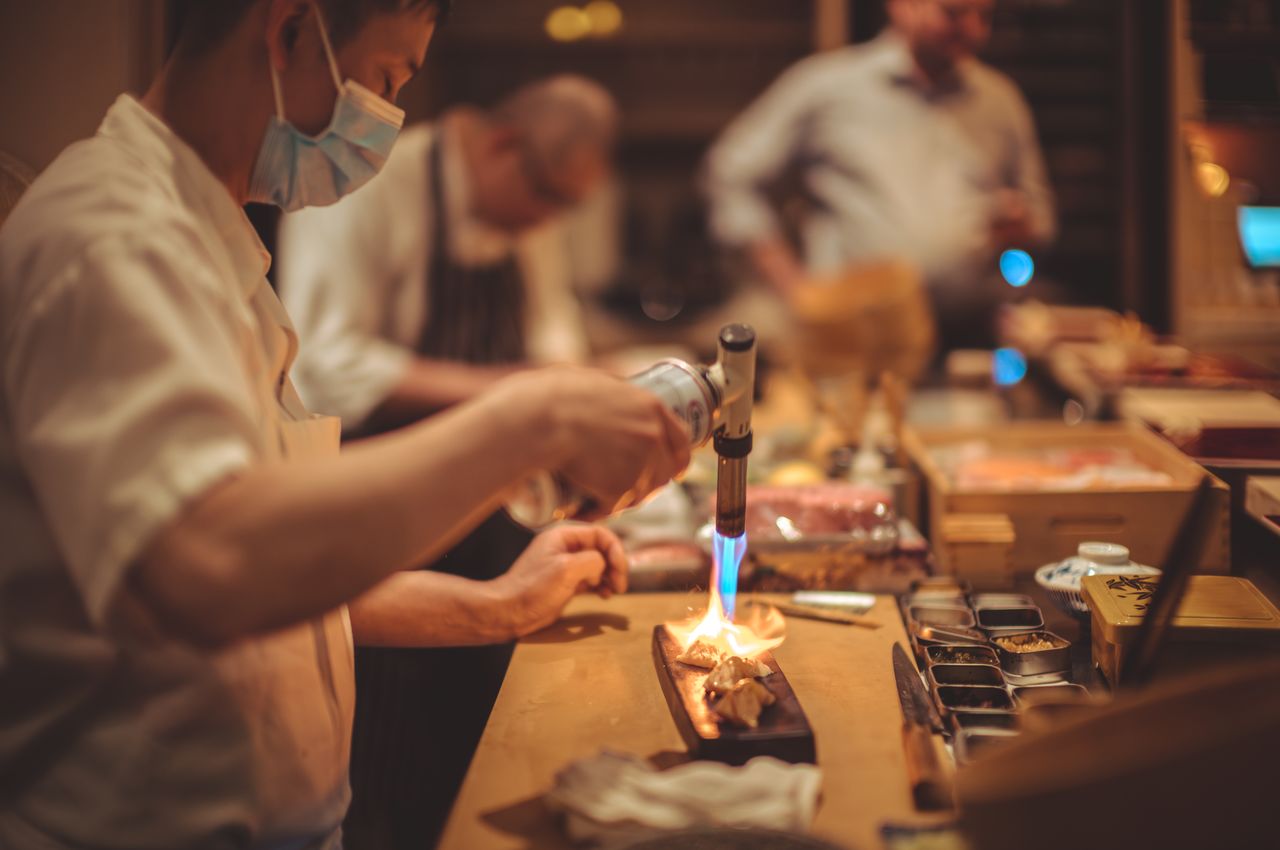 A sushi chef is using a torch to sear sushi.