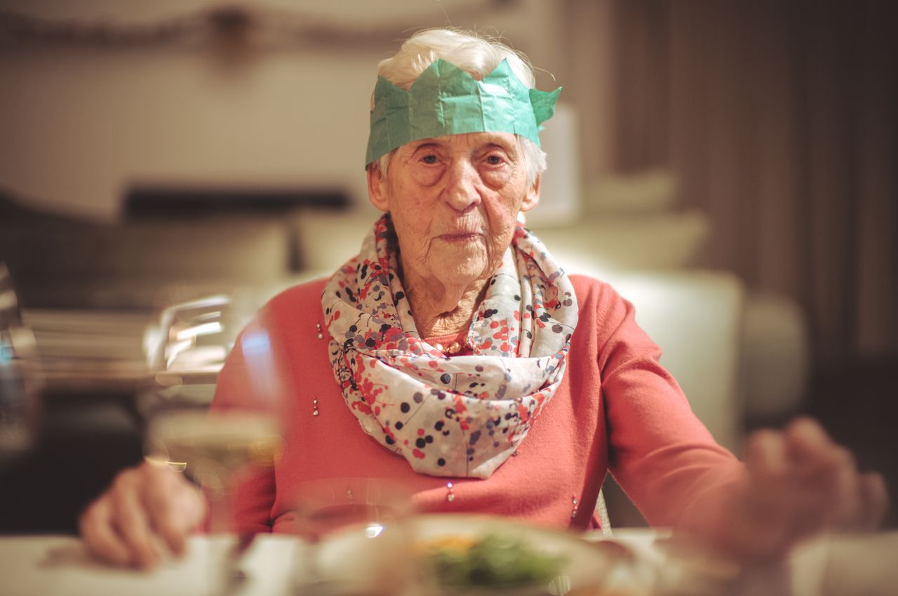 A smiling elderly woman wearing a paper crown.