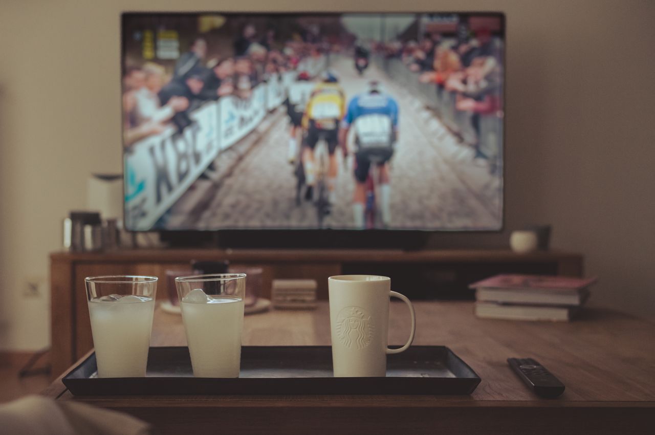 A table with drinks in the foreground and a television showing a cycling race in the background.