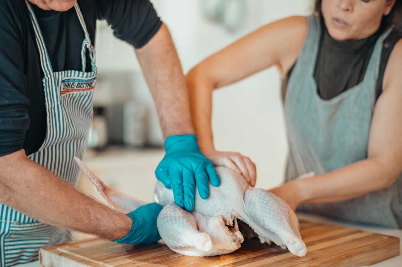 Two people in a kitchen preparing a turkey on a wooden cutting board.
