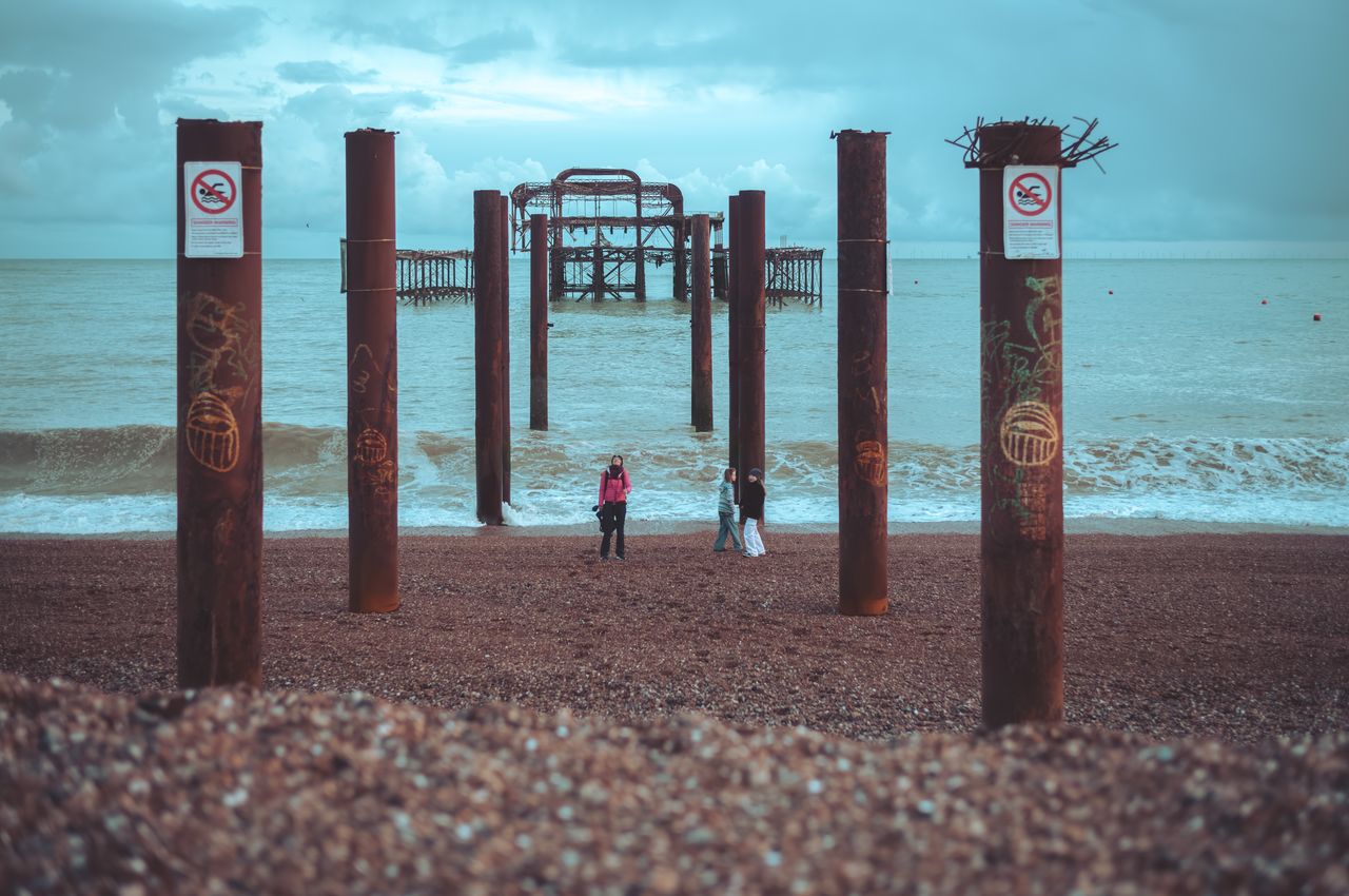 People standing on the beach between the remains of an old pier.