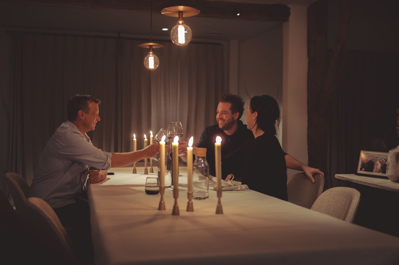 Three people sitting at a dinner table lit by candles, enjoying a glass of wine.