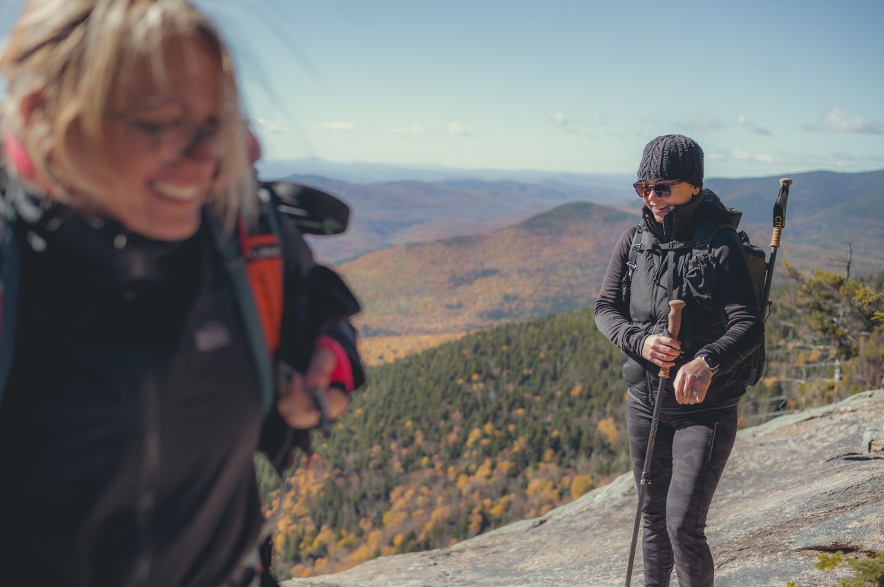 Two hikers on a mountain ledge overlooking the forest.