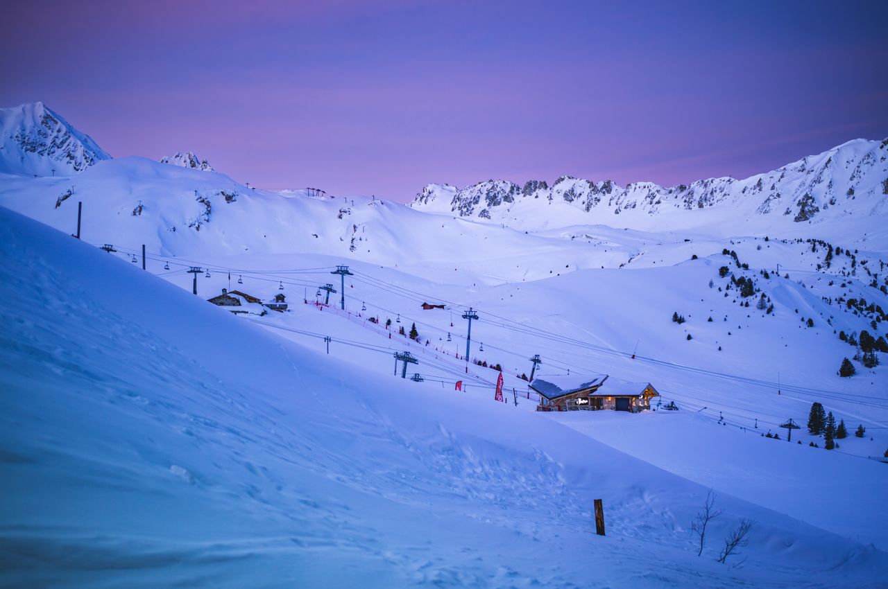 A ski resort at dusk with ski lifts, a small wooden cabin, and a sky with shades of purple and blue.