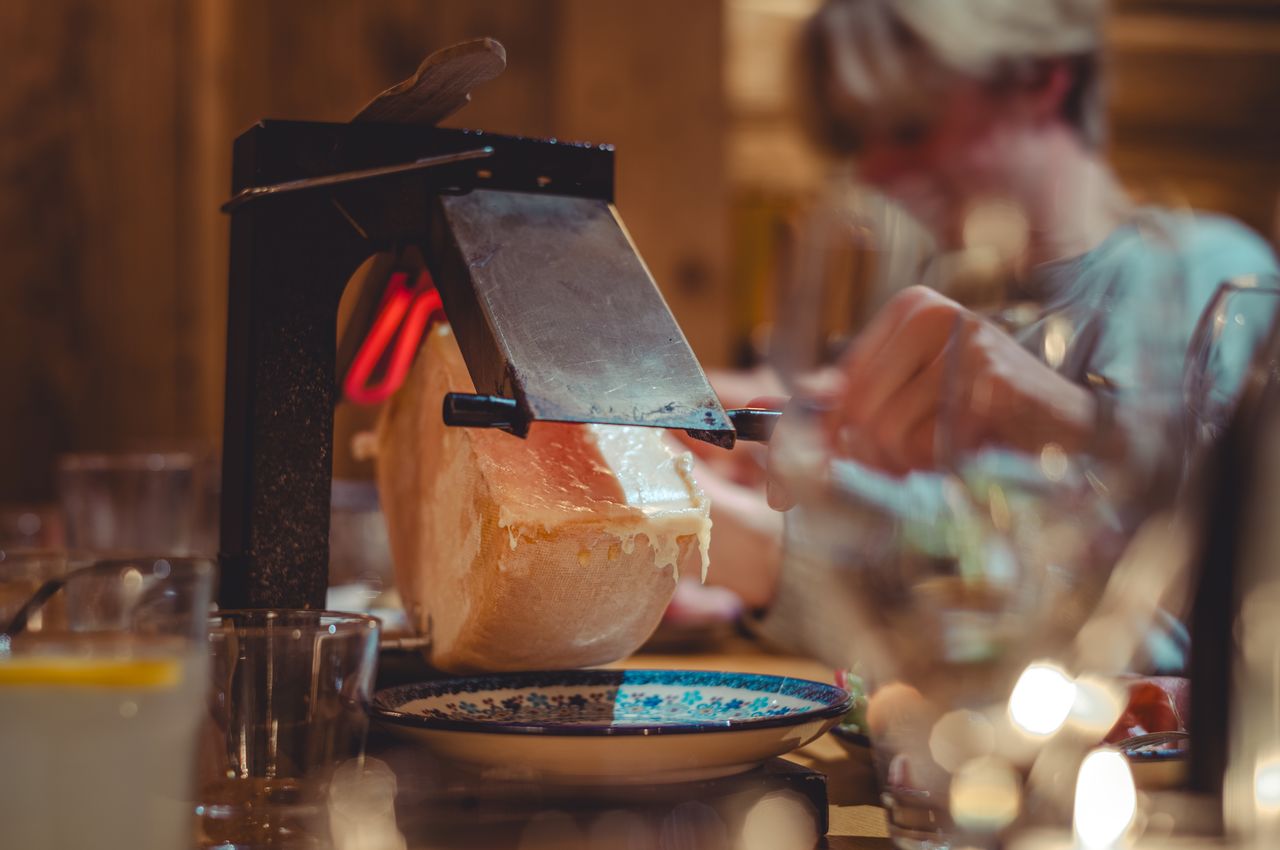 A traditional French raclette grill with melting cheese, scraped onto a plate in a warm, inviting setting.