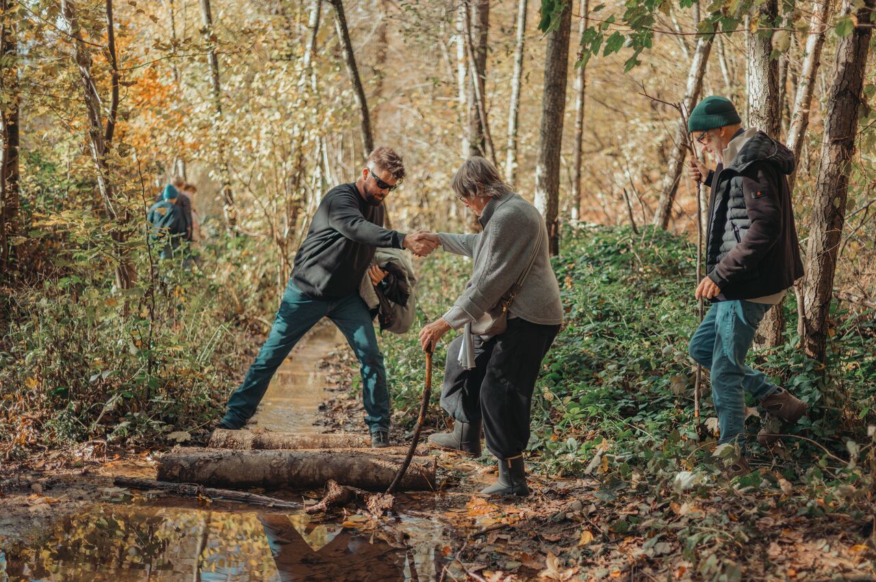 A man helps his parents cross a stream while hiking.