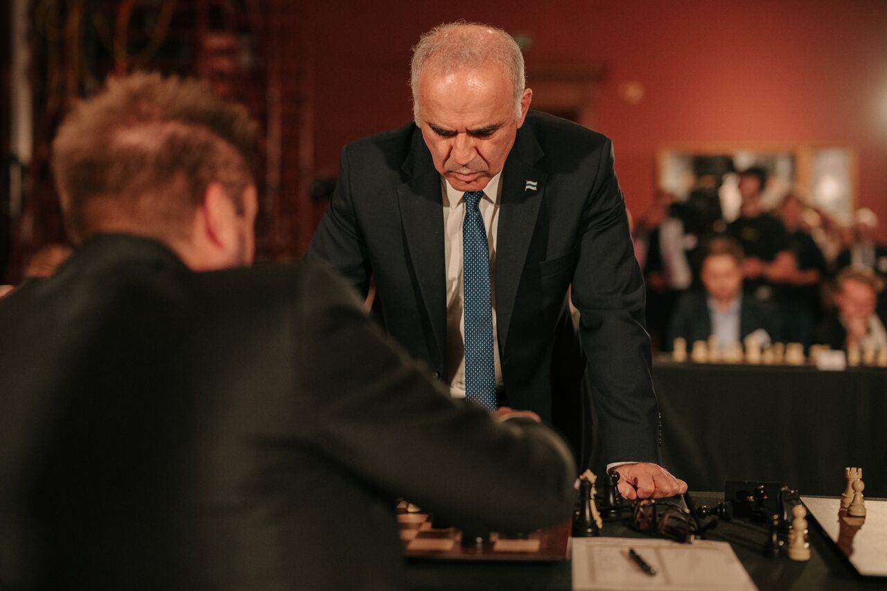 Kasparov stands across the chessboard, focused on his opponent's position.