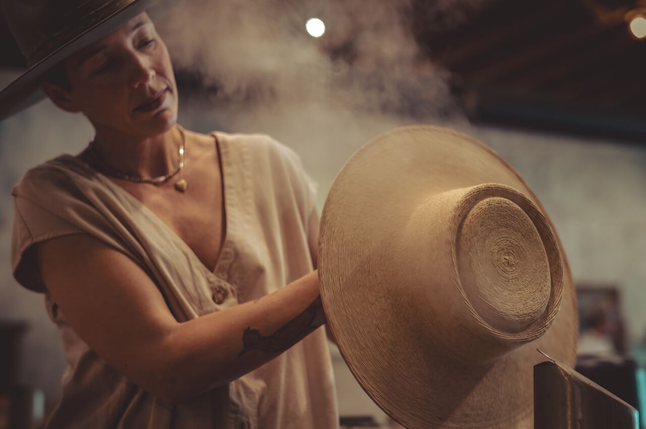 A woman using steam to soften and shape a custom hat.