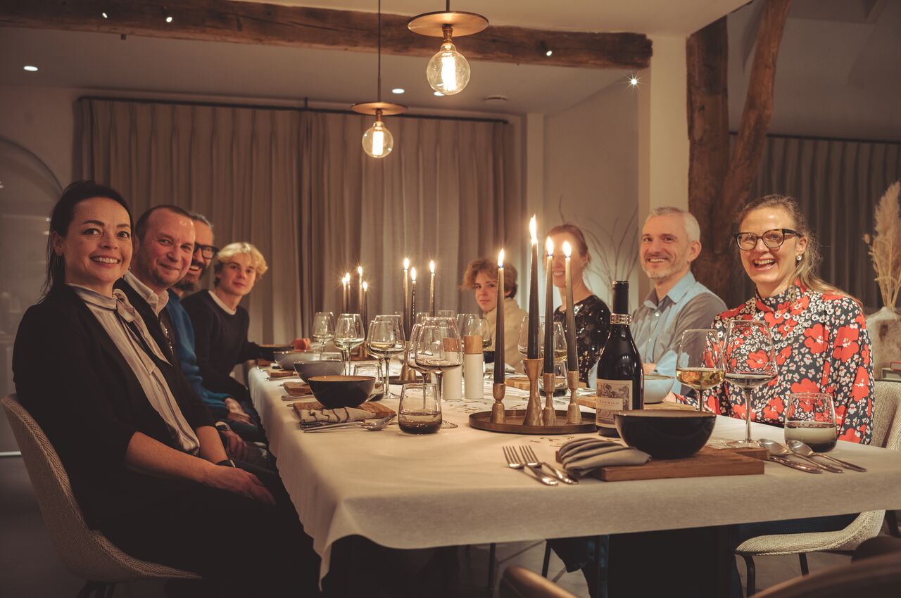 A group of friends and family smiling around a candlelit dinner table, celebrating New Year's Eve in a warm, cozy setting.