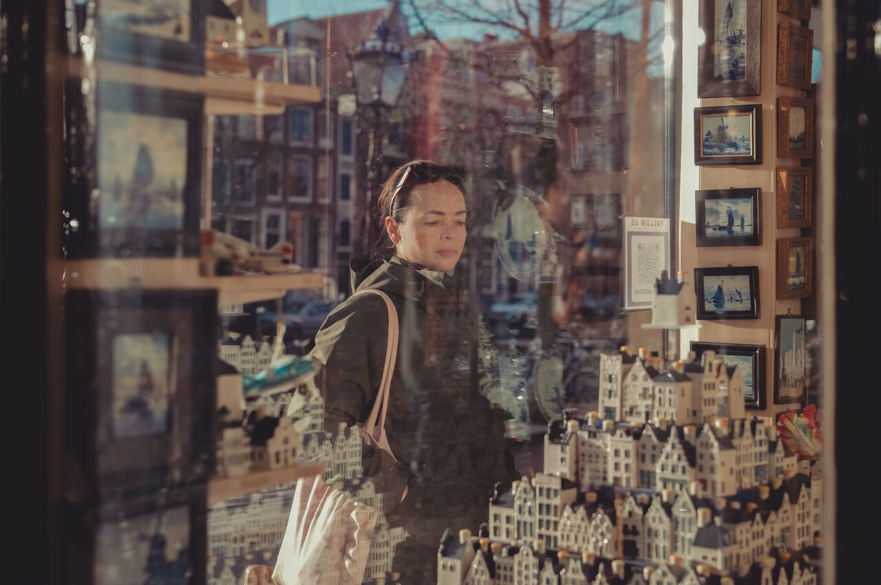 A woman in Amsterdam, seen through a shop window, looking at stone statues of Dutch houses.