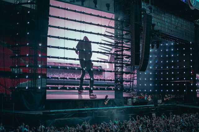 The Foo Fighters perform on a large stadium stage in Liverpool, UK, with a giant video screen showing Dave Grohl.