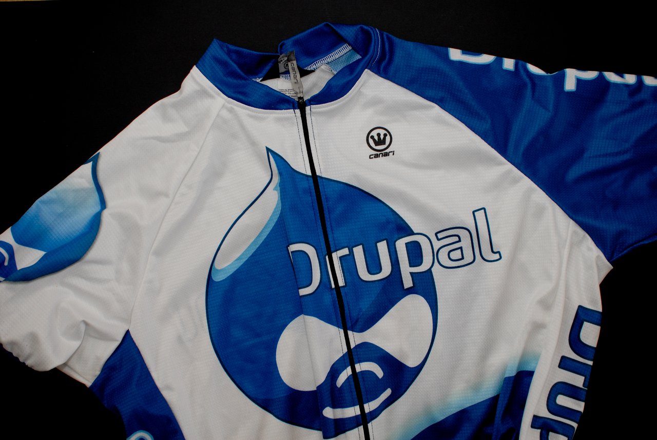 A blue and white cycling jersey with the Drupal logo and branding, laid flat on a black surface.