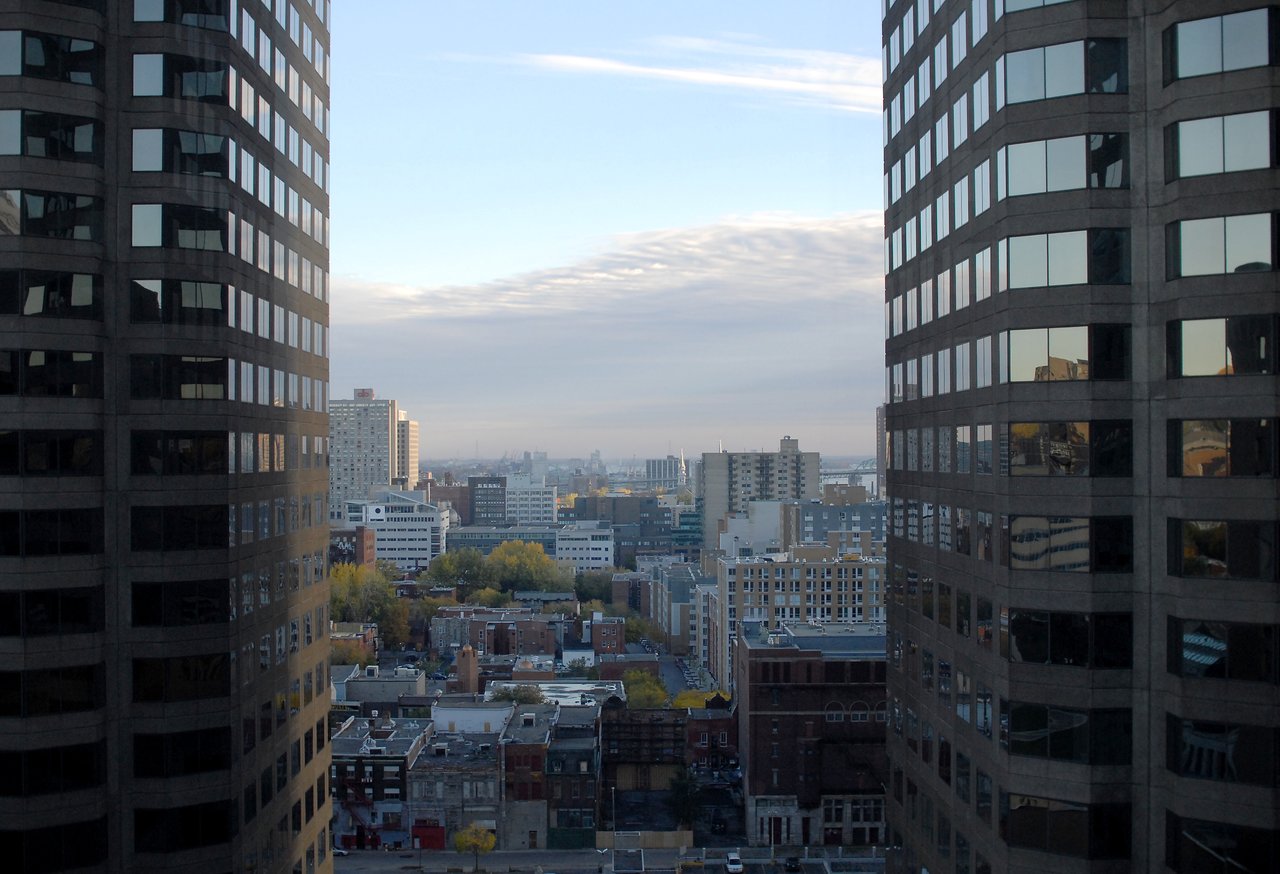 A cityscape view from a high-rise hotel room, framed by two tall office buildings with reflective windows.