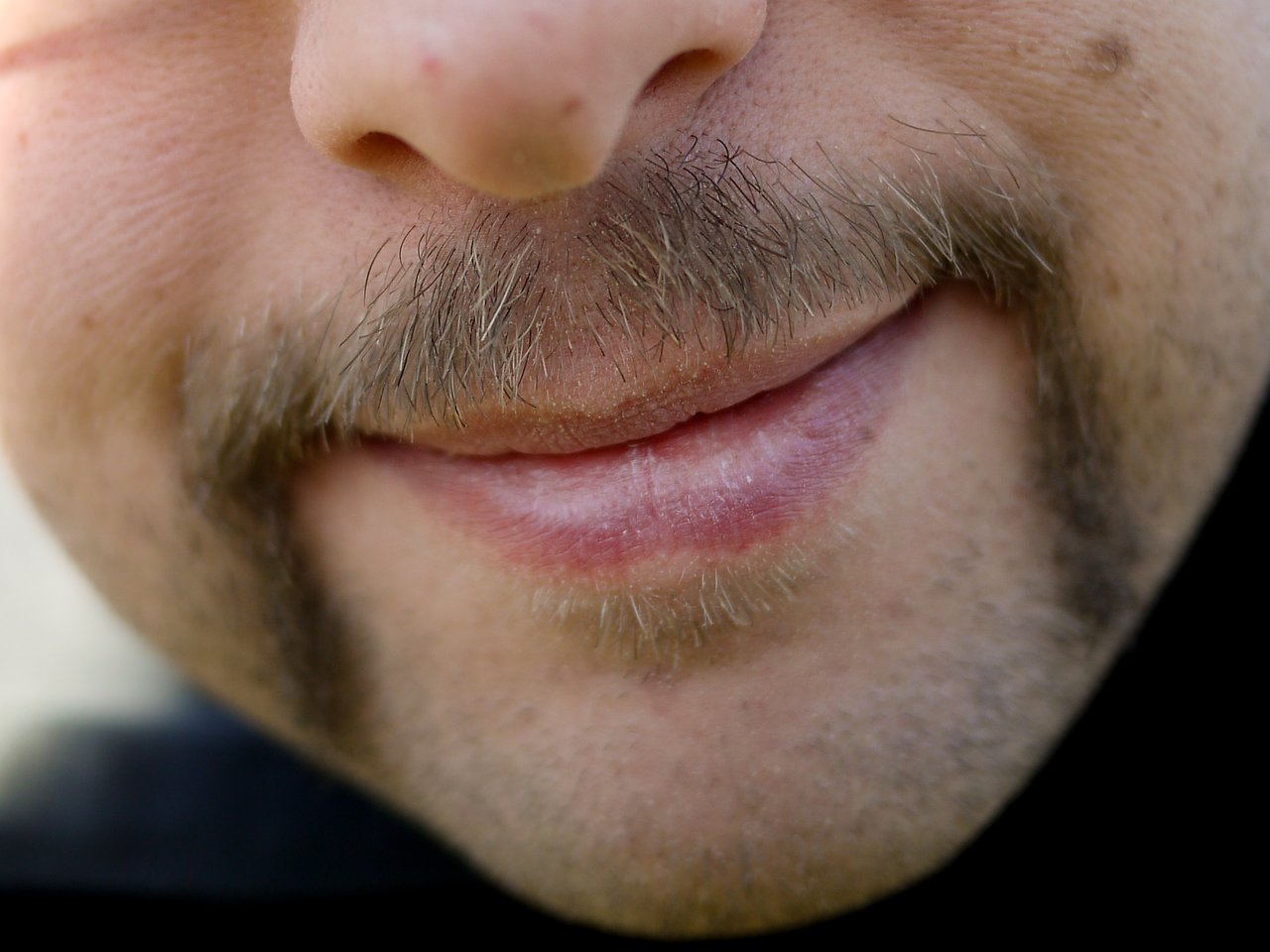 Close-up of a person's face showing a styled mustache grown for Movember, with a slight smile.