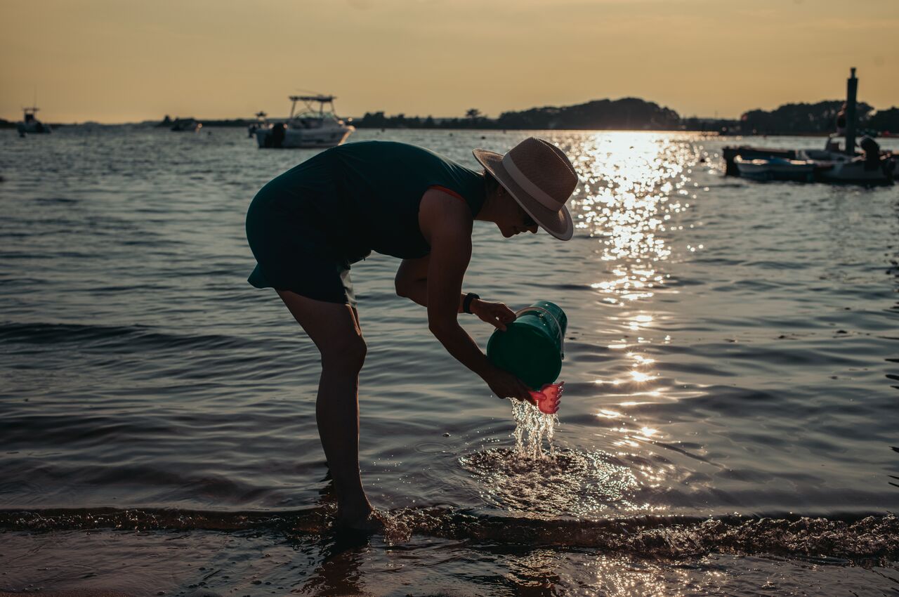 Person in a sunhat pours water from a bucket during sunset.