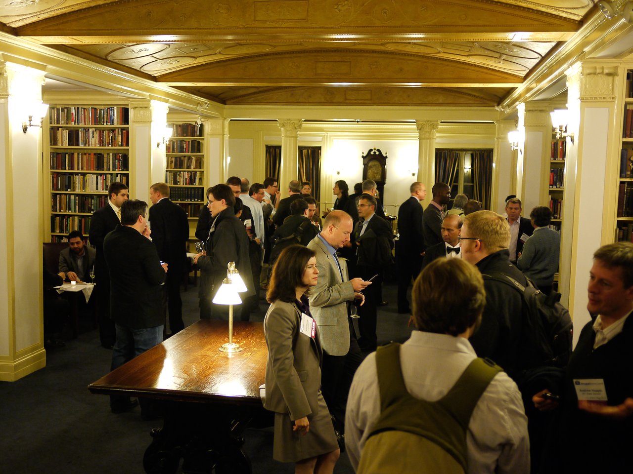 A group of people in business attire networking and conversing at a reception in a library setting.