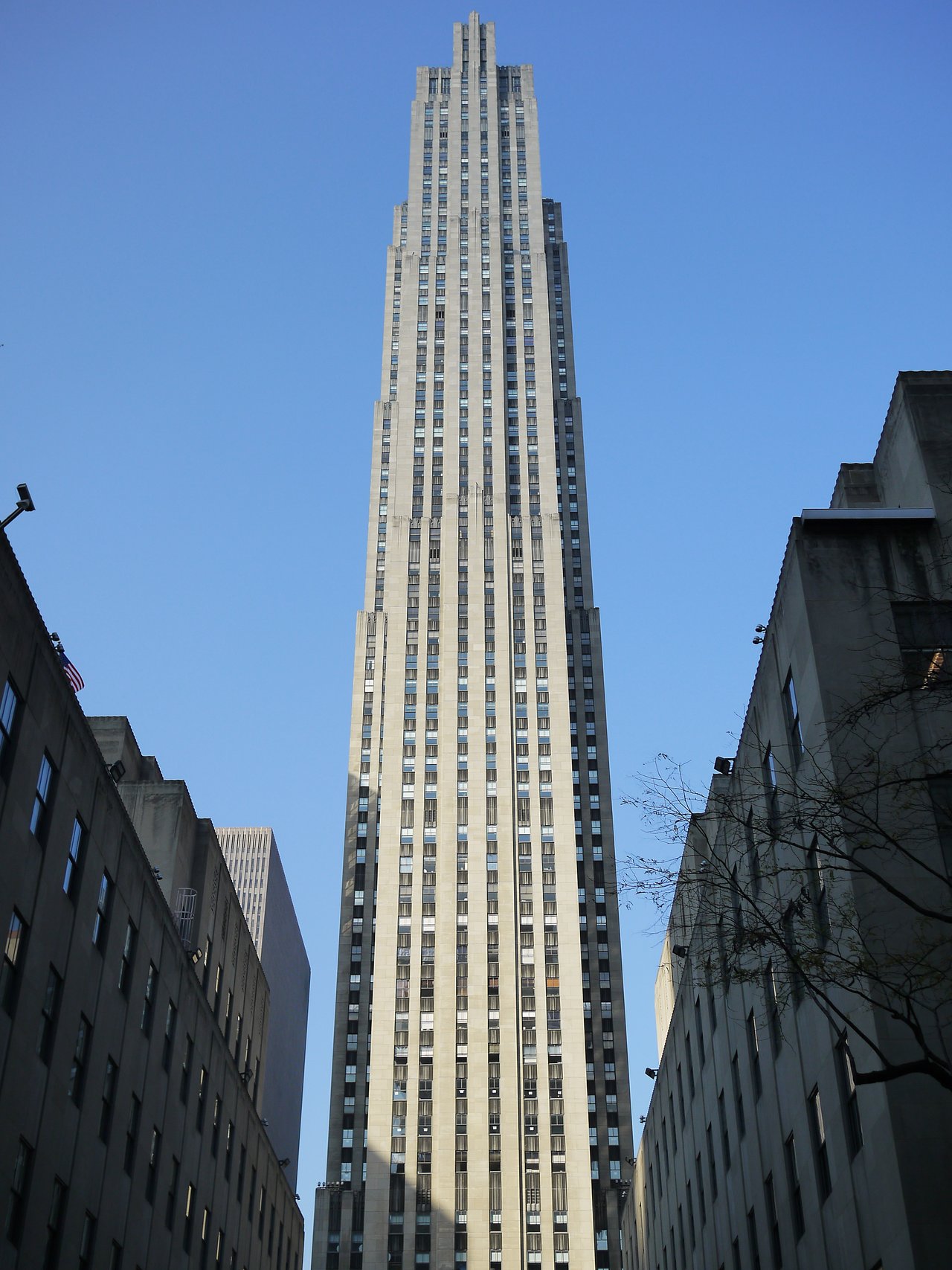 30 Rockefeller Plaza rising against a clear blue sky between two lower buildings.