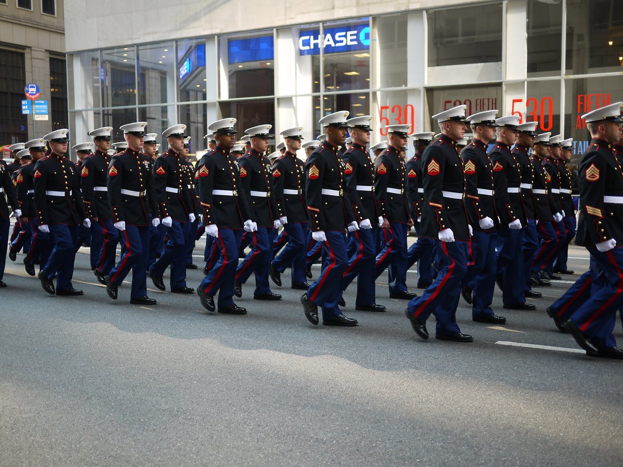 Rows of Marines in dress blues and white caps marching past a Chase bank branch on Fifth Avenue.