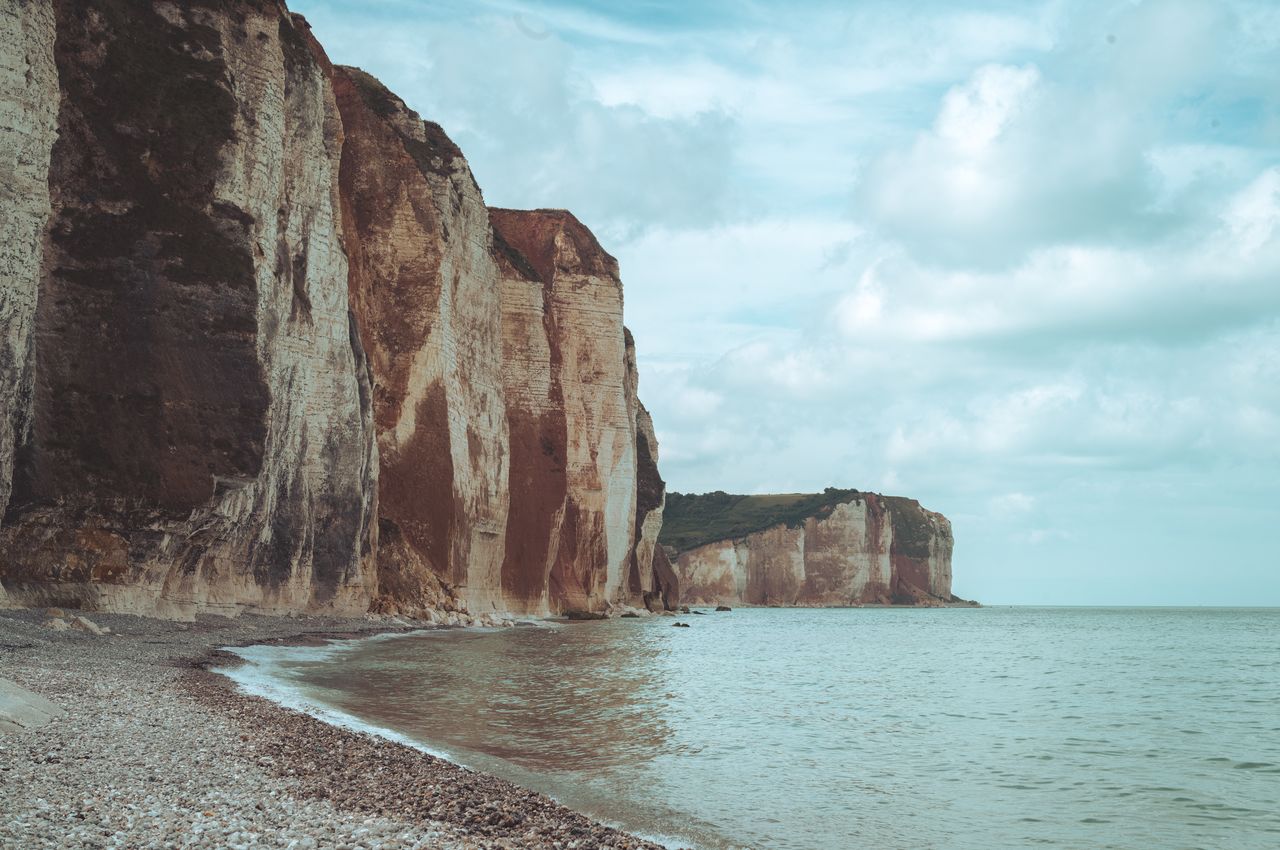 A pebble beach with calm waters in the foreground and towering cliffs extending for miles in the background.