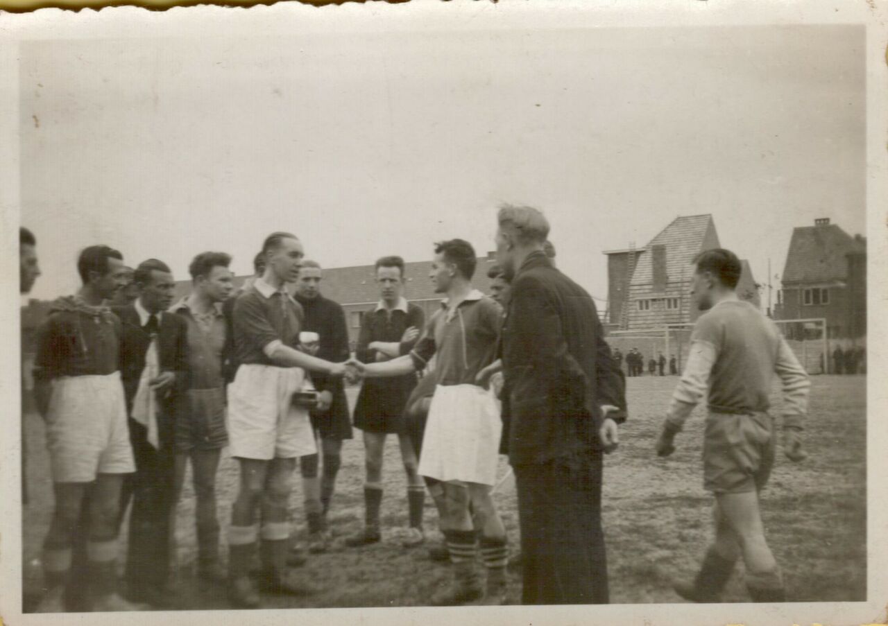 Two soccer team captains shake hands on the field before a match, surrounded by players and officials.