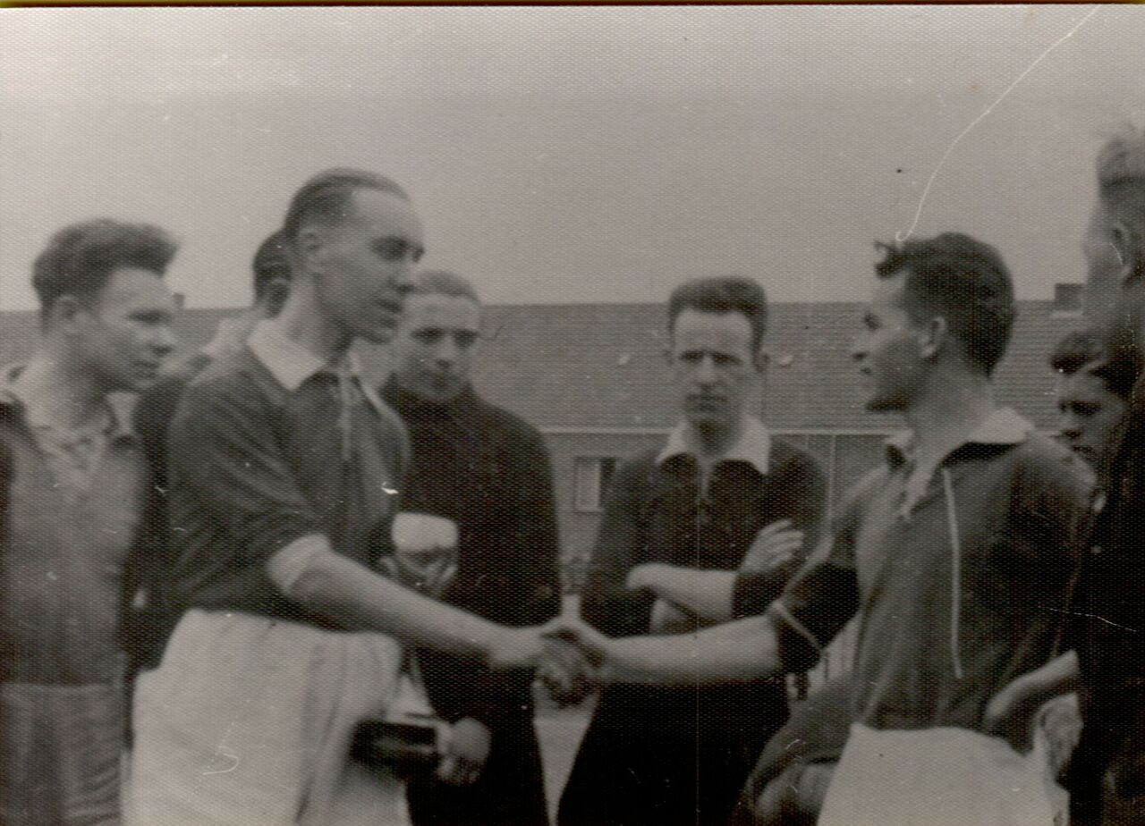 Two soccer captains shake hands on the field before a match, surrounded by teammates and officials.