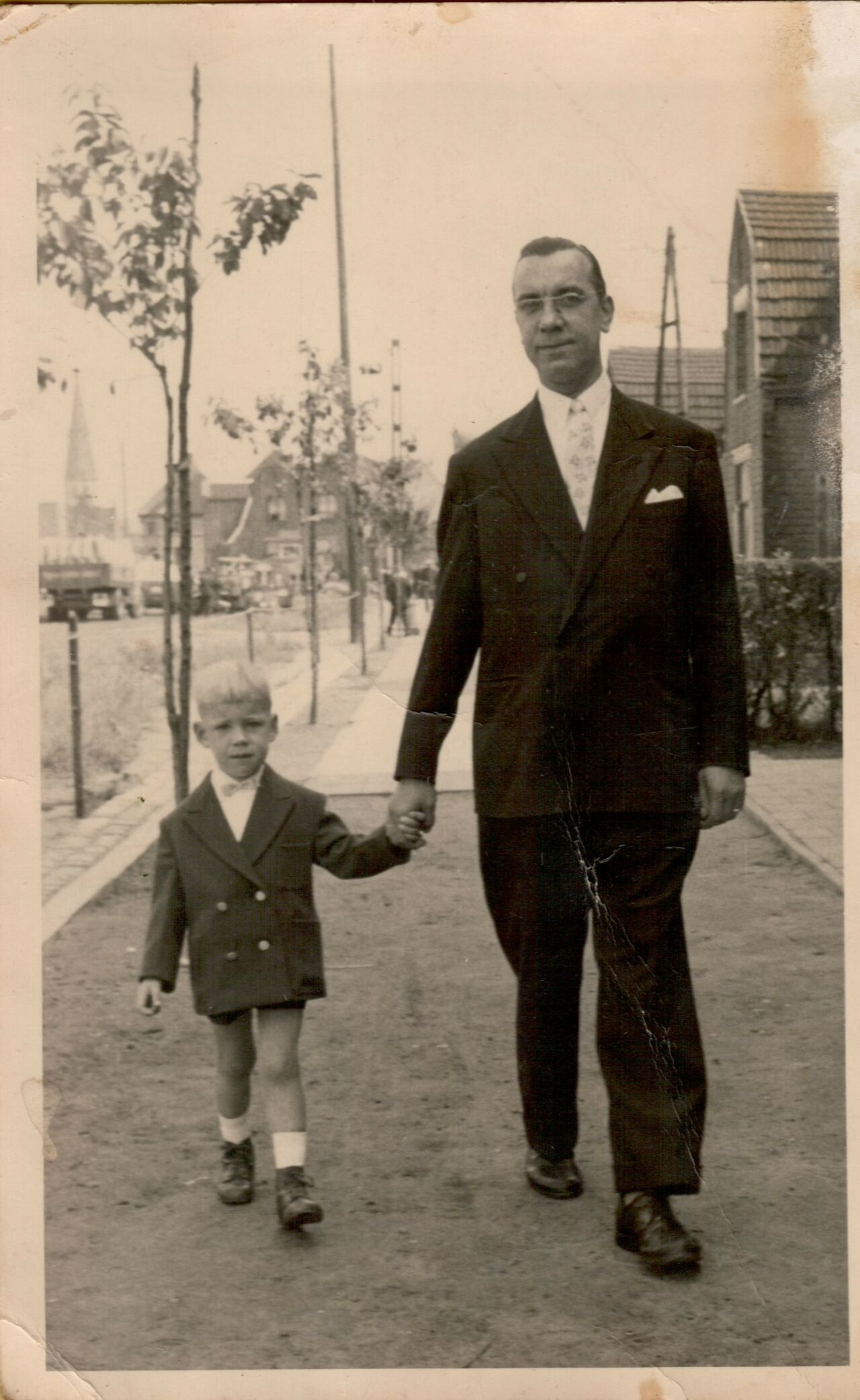 A man in a suit walks down a path holding hands with a young boy in a jacket.