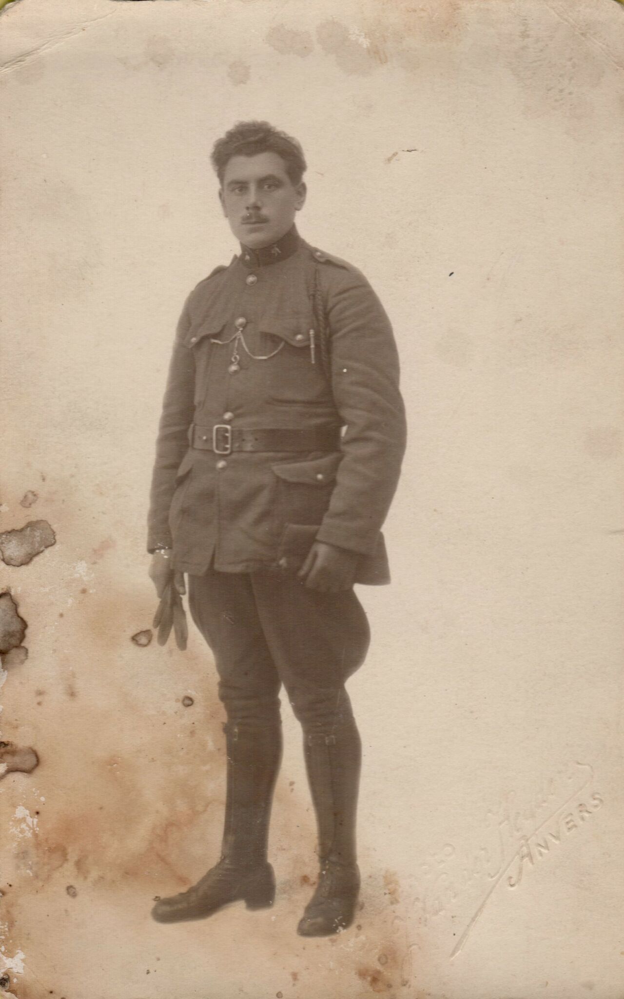 A man in a military uniform stands for a portrait, holding gloves in one hand.