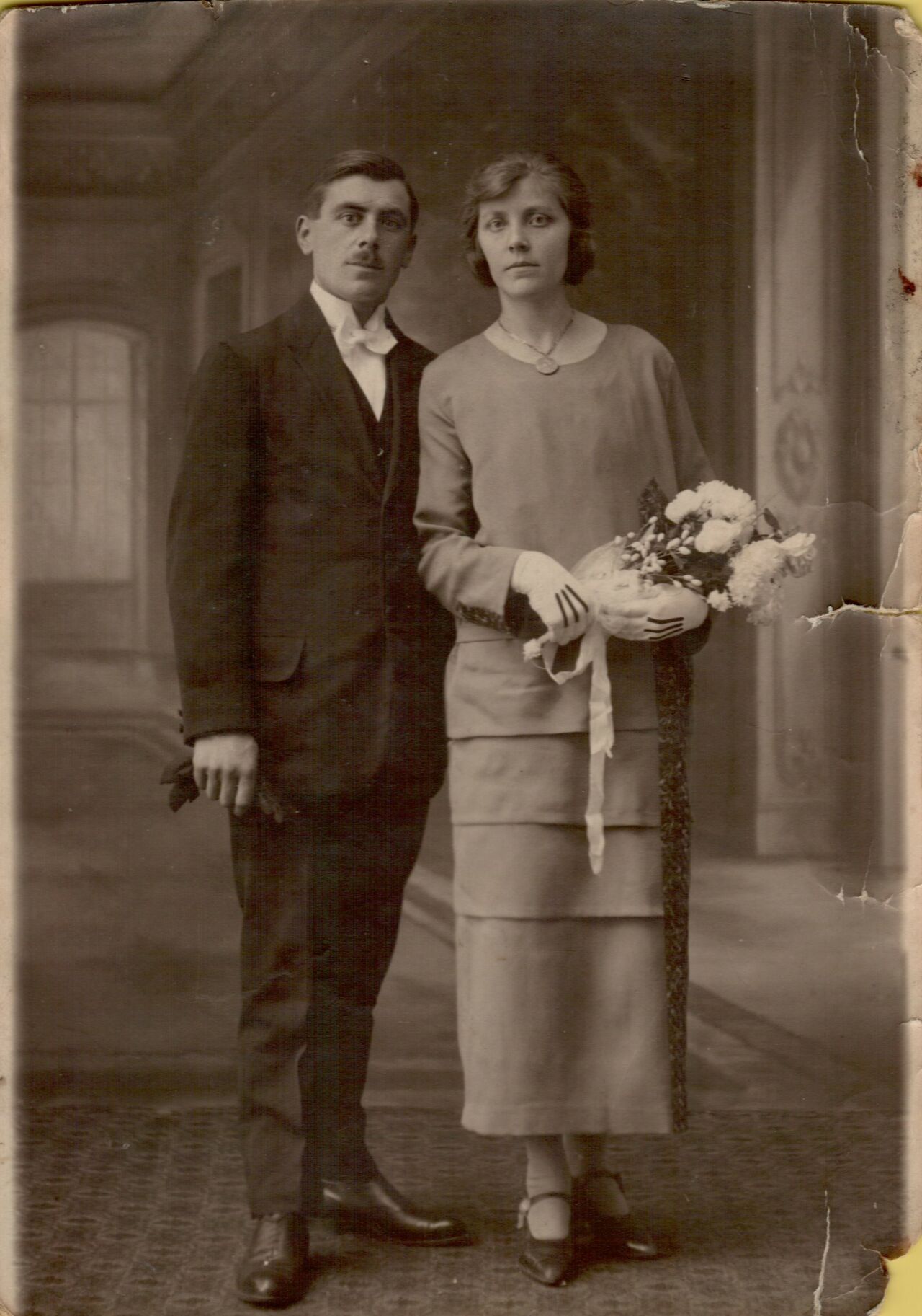 A man in a suit and a woman in a dress stand side by side, holding flowers.