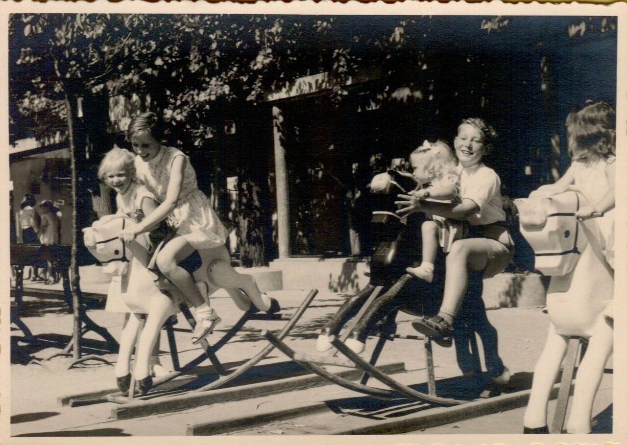 Two women ride playground rocking horses with young children, all smiling and enjoying the moment.