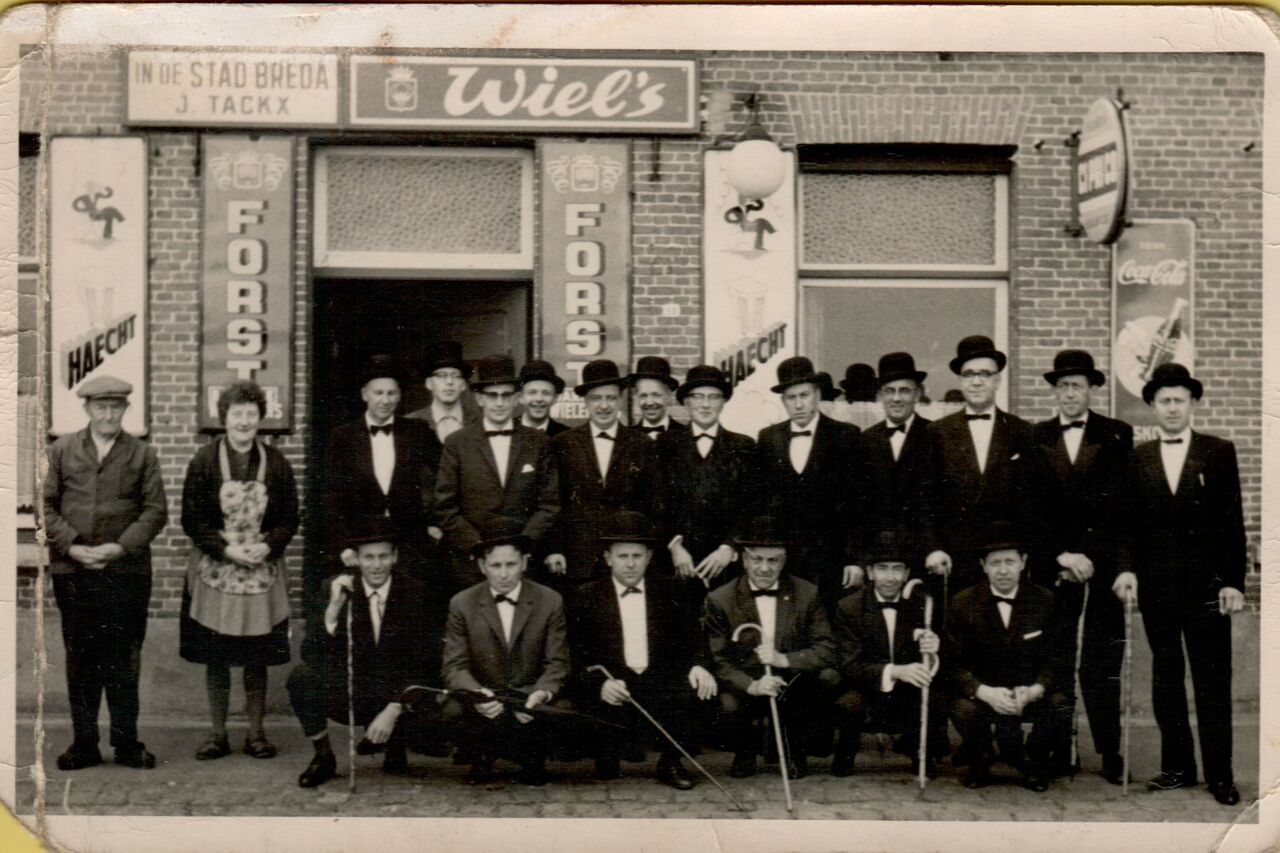 A group of men in suits and bowler hats pose in front of a brick building, with two others nearby.